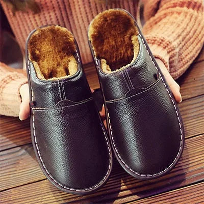 Close-up of black leather mule slippers with fleece lining, held by hand showing fluffy brown interior and stitched trim.