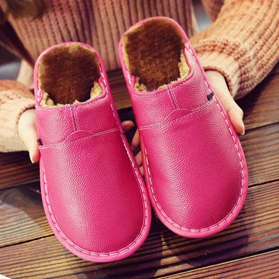 Pink leather mule slippers with soft fleece interior, held in hands to show the padded sole and stitched edge.