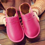 Pink leather mule slippers with soft fleece interior, held in hands to show the padded sole and stitched edge.