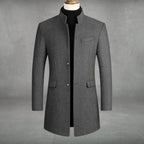 Grey wool-blend overcoat with stand collar, single-breasted button front and flap pockets, shown on mannequin with black polo neck jumper