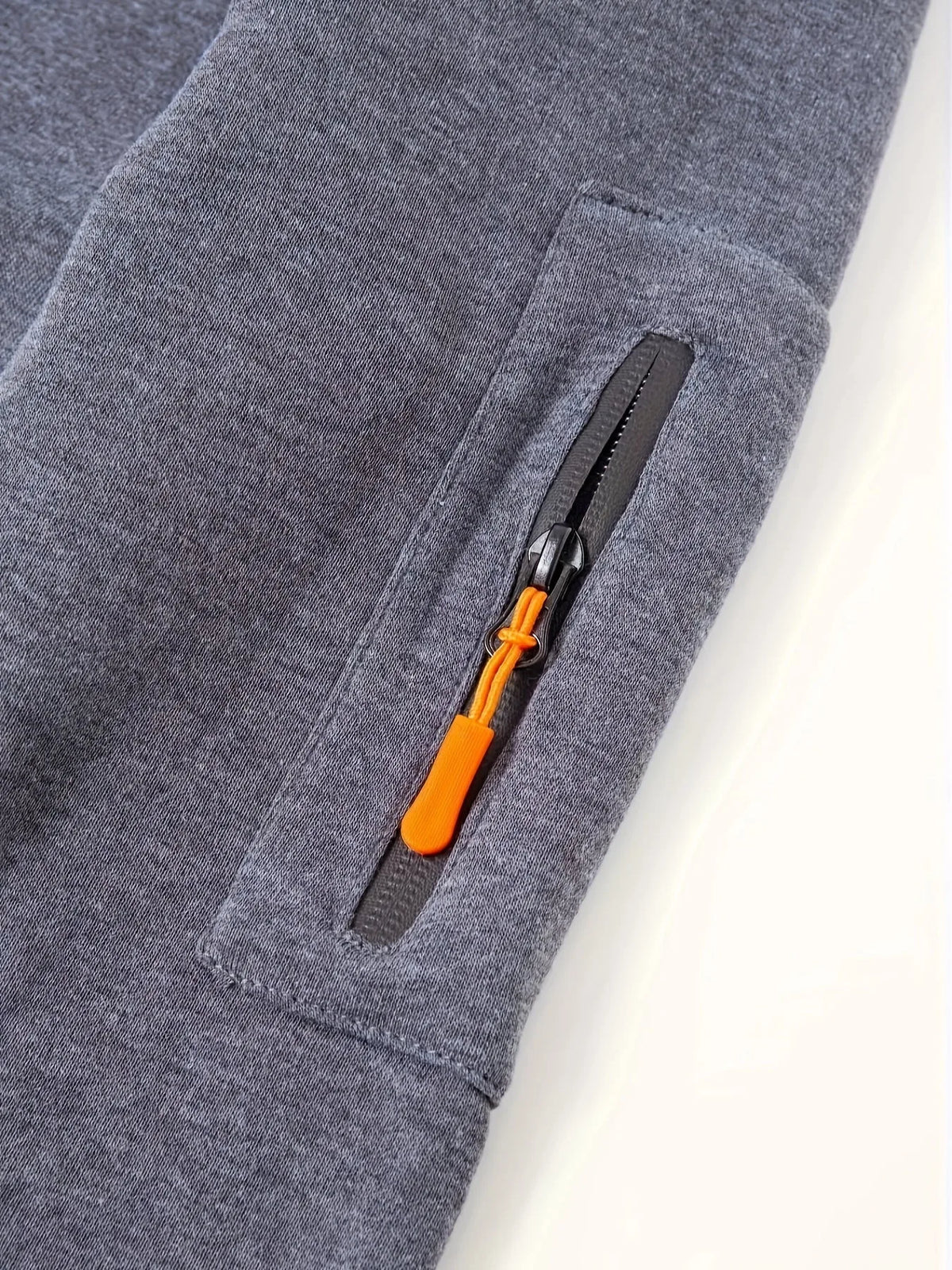 Close-up of front pocket with orange zip pull and ribbed cuff detail on grey hoodie