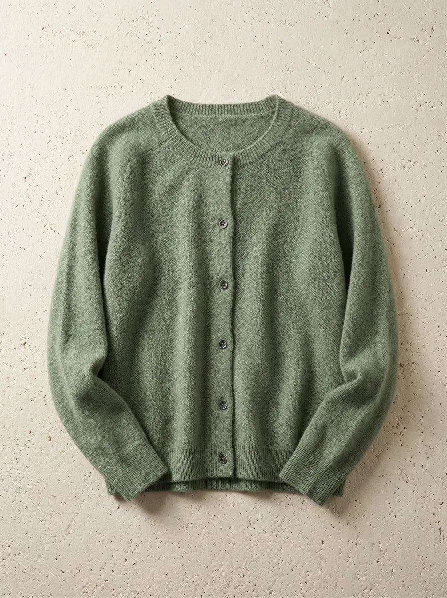 Sage green cardigan with raglan sleeves and ribbed hem, buttoned up and photographed flat on a stone surface