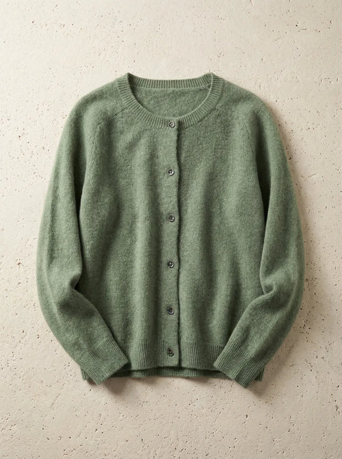 Sage green cardigan with raglan sleeves and ribbed hem, buttoned up and photographed flat on a stone surface