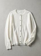 Ivory white cardigan with ribbed cuffs and button placket, laid flat on a neutral grey surface