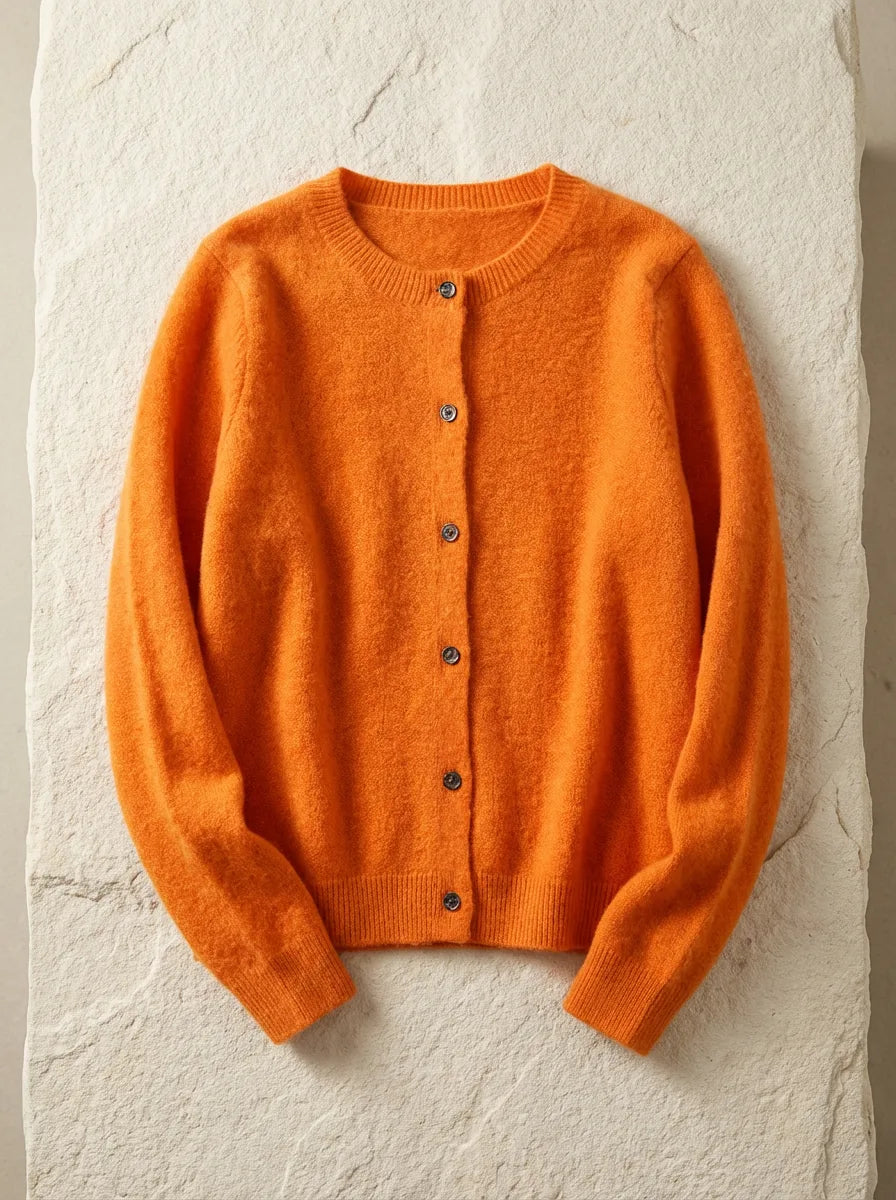 Burnt orange cardigan with textured knit and ribbed trims, laid flat on a pale stone surface