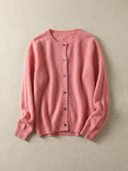 Coral pink cardigan with round neck and tortoiseshell buttons, shown flat on a soft grey background
