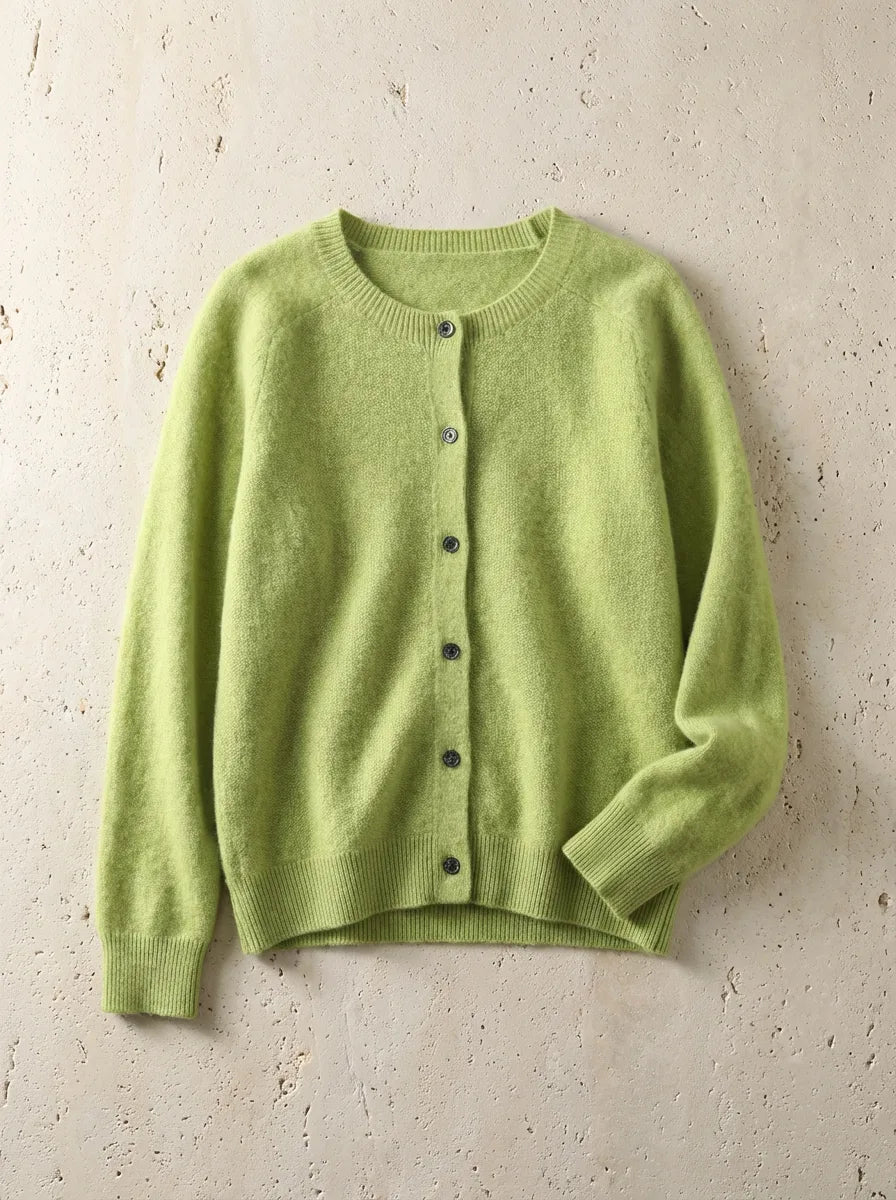 Lime green cardigan with raglan sleeves and ribbed hem, laid flat on a warm beige stone surface