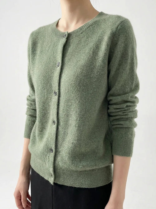 Angled view of a sage green knitted cardigan showing the ribbed cuffs and round neckline on a model