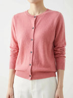 Front view of a dusty pink knitted cardigan with dark buttons, worn with cream trousers
