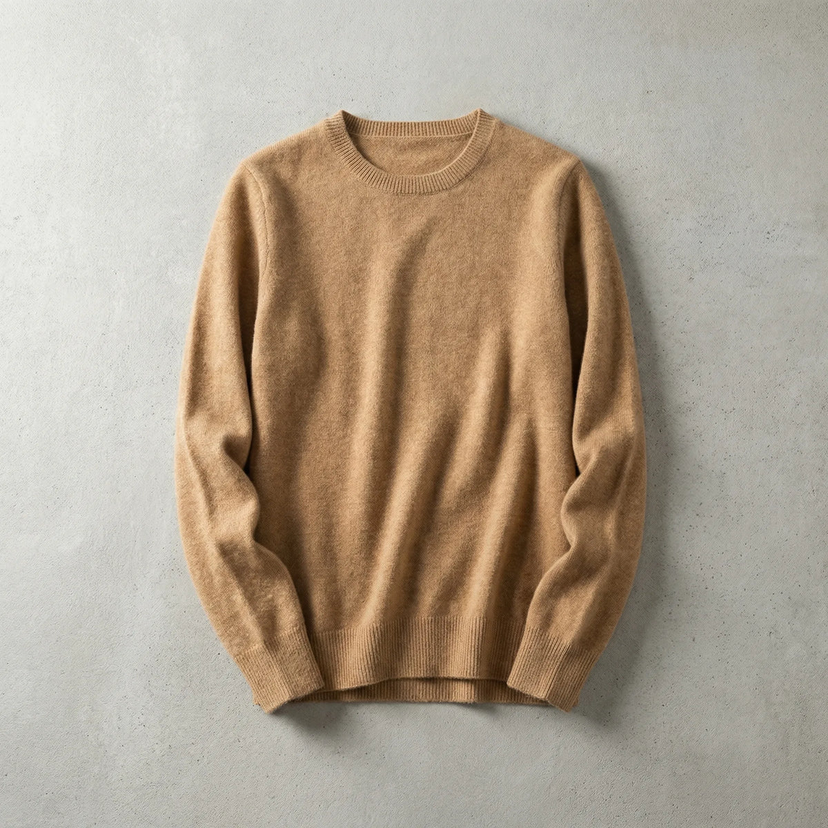 Folded camel brown merino wool jumper with ribbed crew neckline laid flat on a light grey surface
