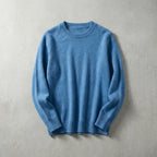Folded sky blue merino wool jumper showing ribbed cuffs and crew neck, laid flat on a grey backdrop