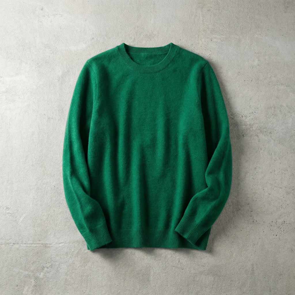 Folded emerald green merino wool jumper with ribbed collar, laid flat against a concrete grey wall