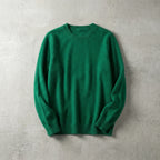 Folded emerald green merino wool jumper with ribbed collar, laid flat against a concrete grey wall