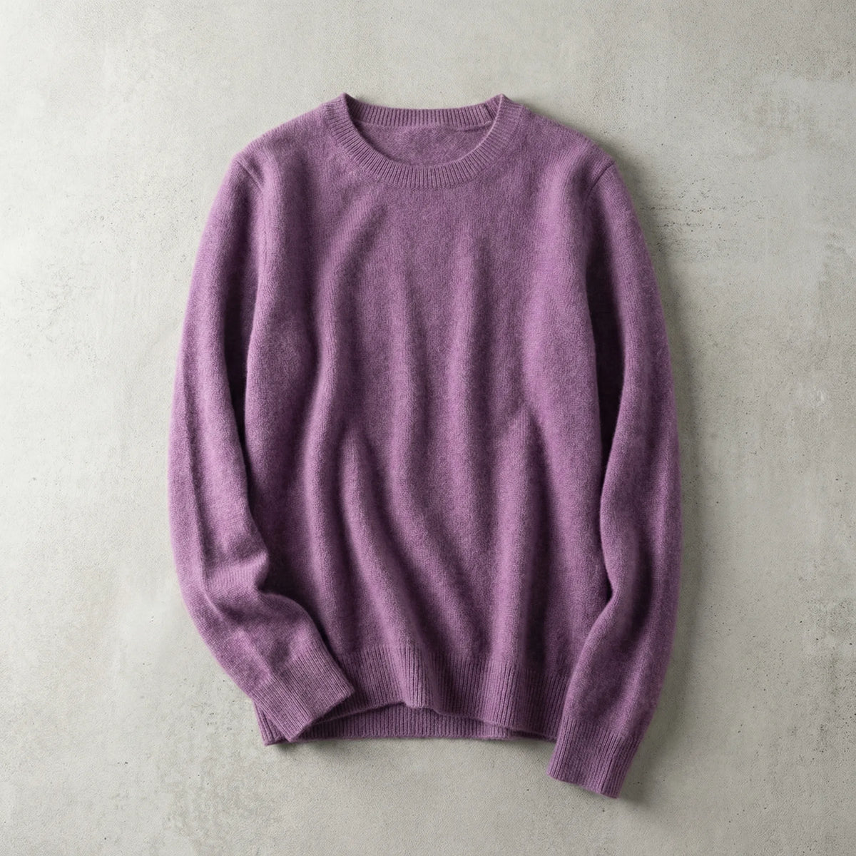 Folded mauve purple merino wool jumper with ribbed cuffs, laid flat on a soft grey surface