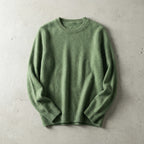 Folded sage green merino wool jumper with ribbed crew neckline, laid flat on a textured grey backdrop