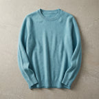 Folded pale blue merino wool jumper with ribbed hem and cuffs, laid flat on a warm beige backdrop