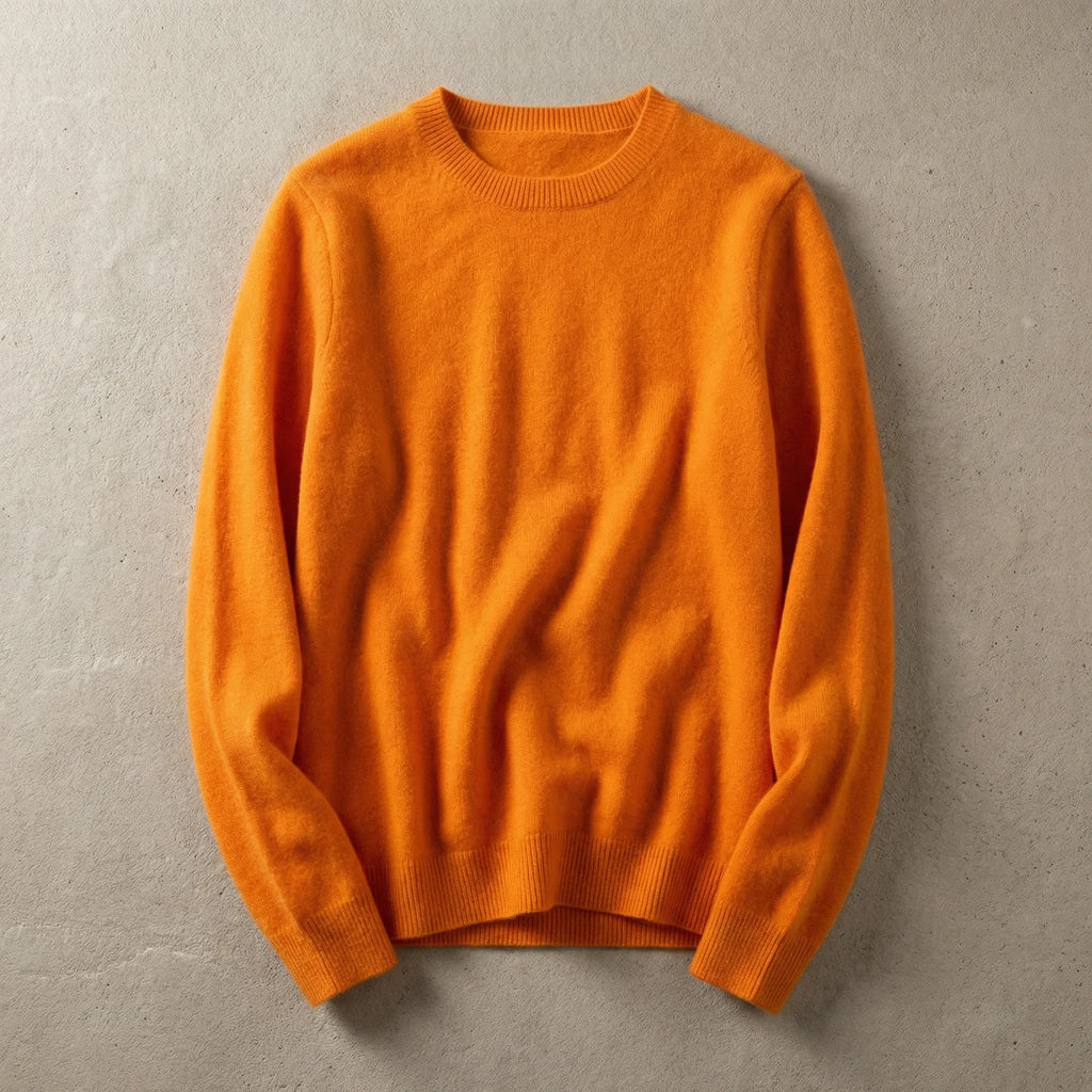 Folded bright orange merino wool jumper with ribbed neckline and cuffs, laid flat on a grey surface