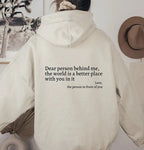 Model wearing an oversized cream hoodie from behind, showing the full back print and drawstring hood