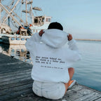 Back view of a white oversized hoodie worn on a wooden pier, showing the lowercase back message in full