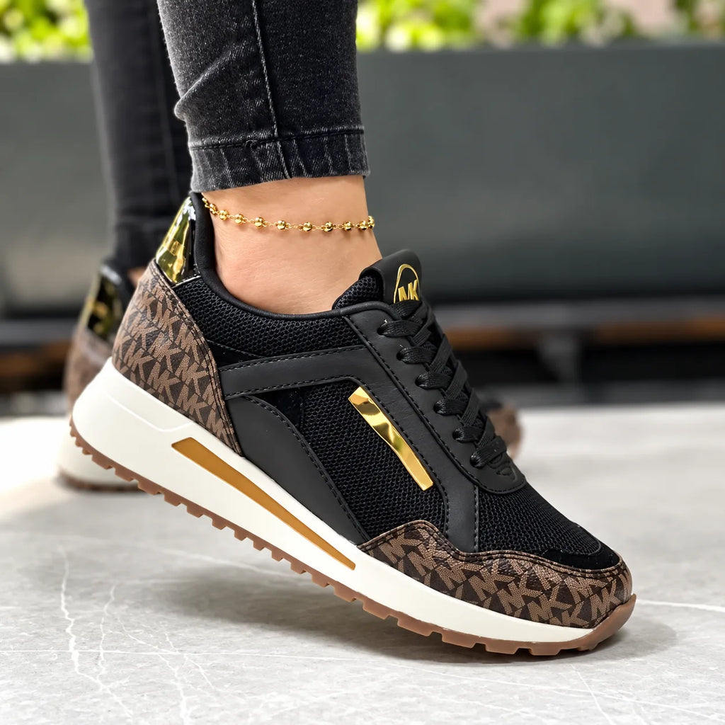Close-up side view of brown monogram print trainer with black mesh panels and gold metallic heel and lace trims, worn on foot