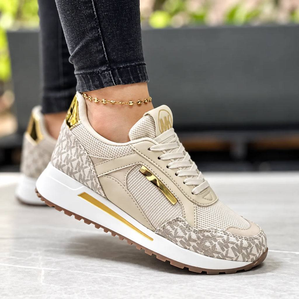 Beige monogram print trainer with cream leather panels, mesh detailing and gold heel accent, shown on model's ankle