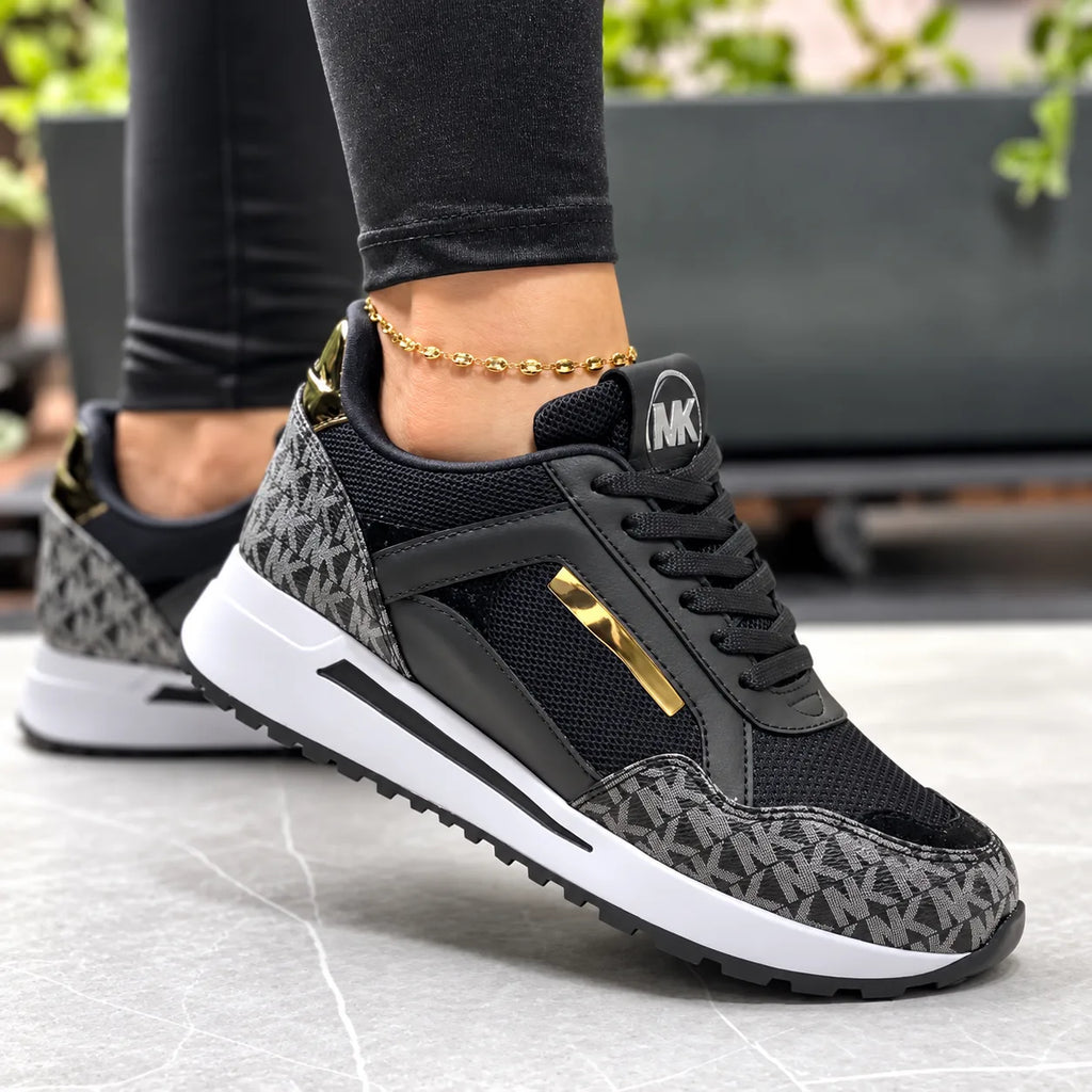 Black and grey monogram print trainer with black mesh panels and gold heel and lace accents, close-up on foot