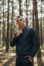 Man adjusting the collar of his navy bomber jacket, highlighting the red, white and navy stripe detail.