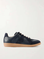 Side view of a navy leather and suede trainer with panelled upper, cream laces and a gum rubber sole