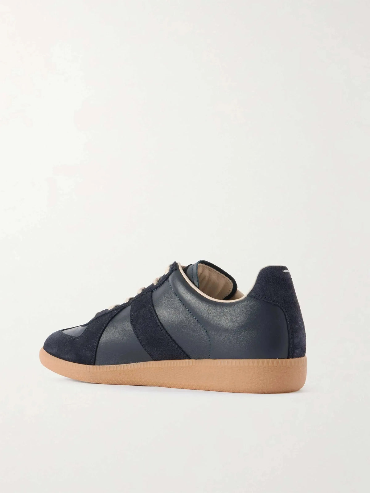 Angled rear-side view showing the heel tab and contrast stitching on the navy leather and suede trainer