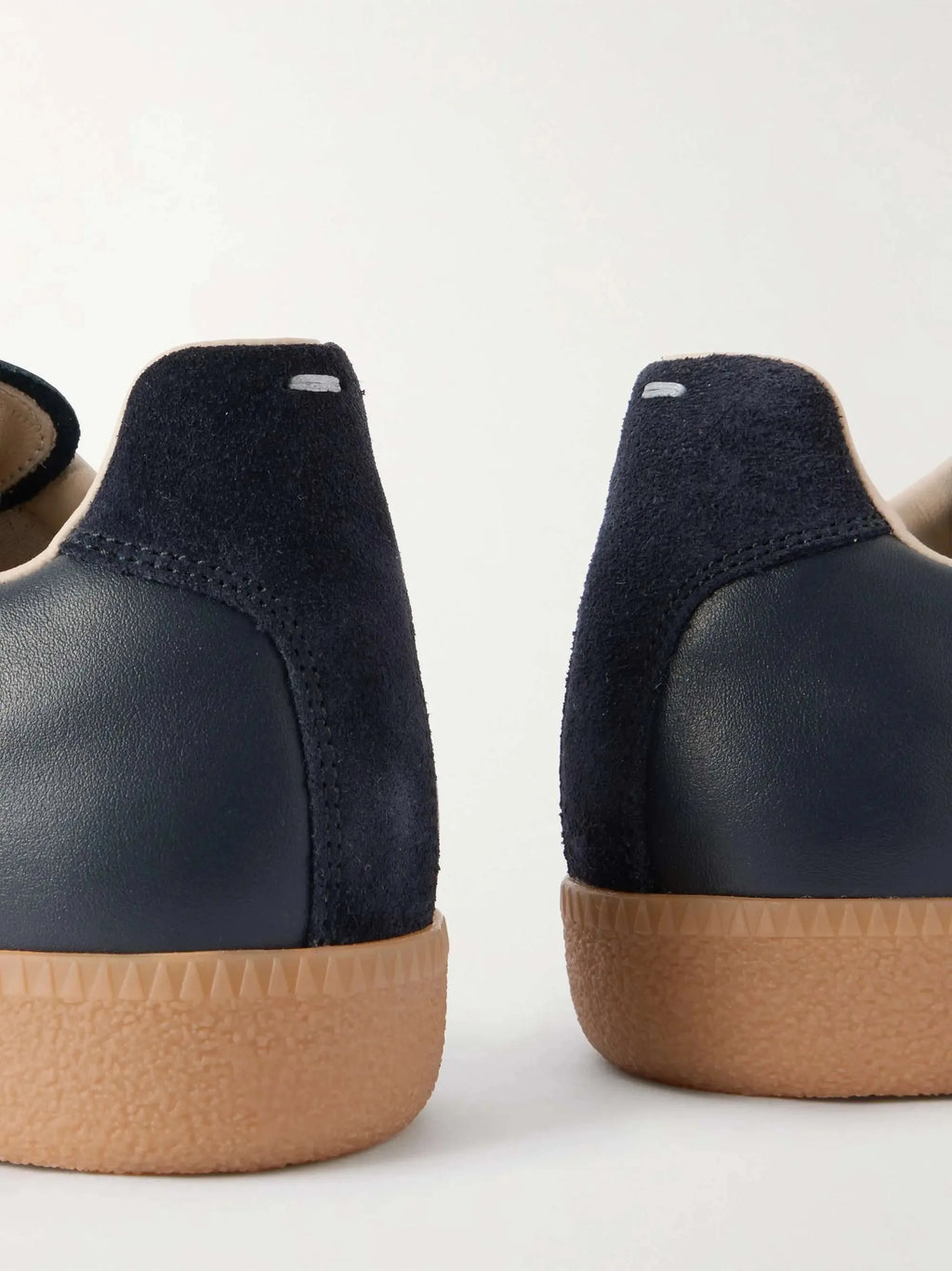 Close-up of two navy suede heel counters with tonal stitching above a ridged gum rubber outsole