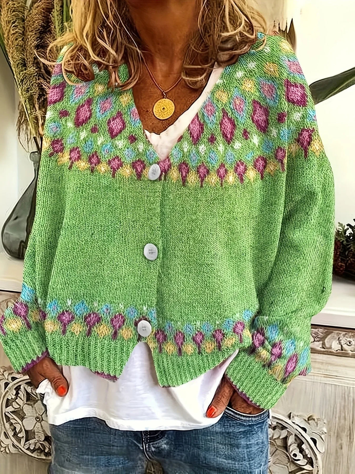 Close-up front view of a green patterned knit cardigan with V-neck, white buttons and Fair Isle yoke, worn over a white top