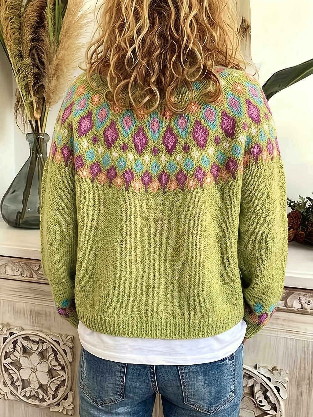Back view of a model wearing the green cardigan, showing the patterned yoke across the shoulders and curly hair
