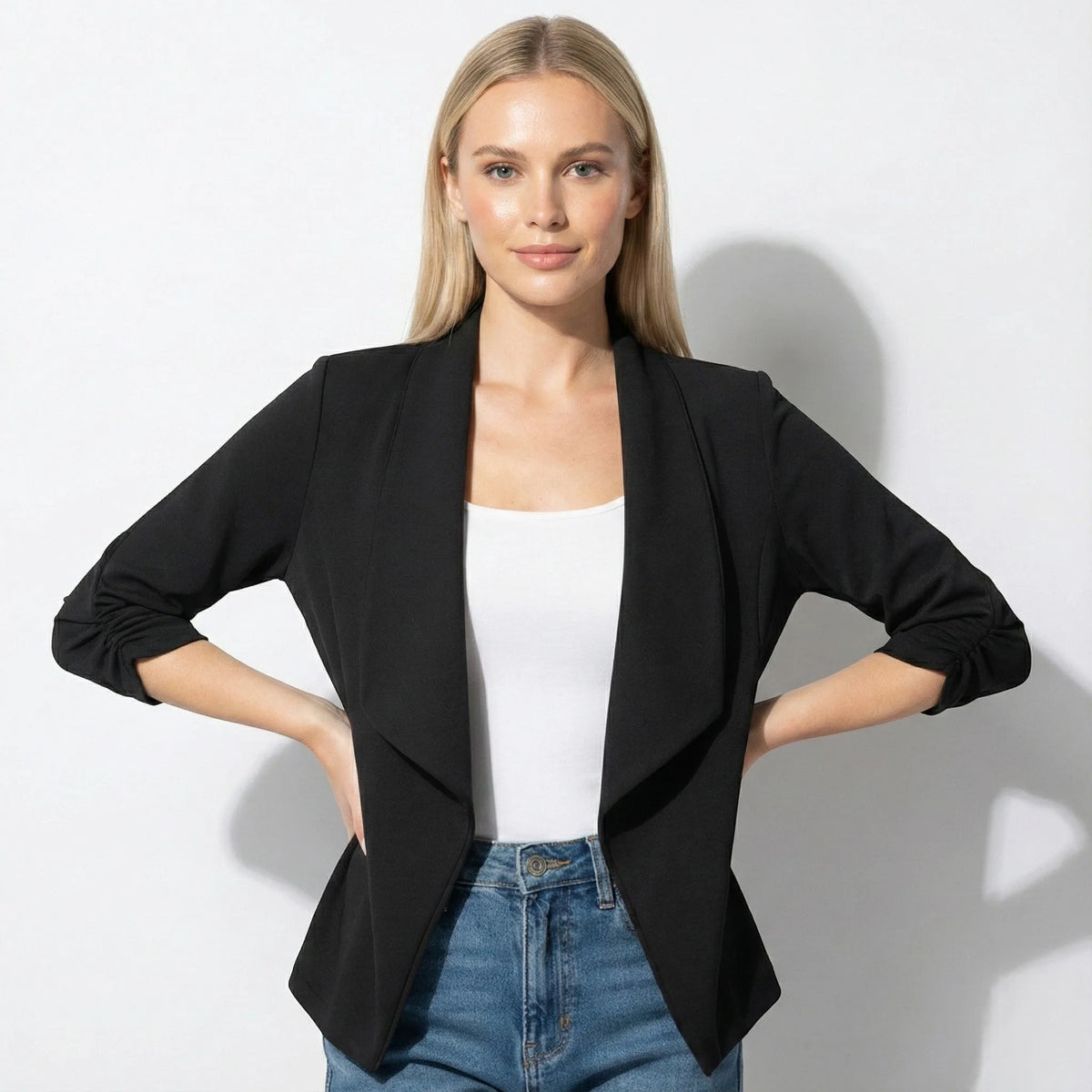 Woman wearing black open-front blazer over a white top, hands on hips, front view