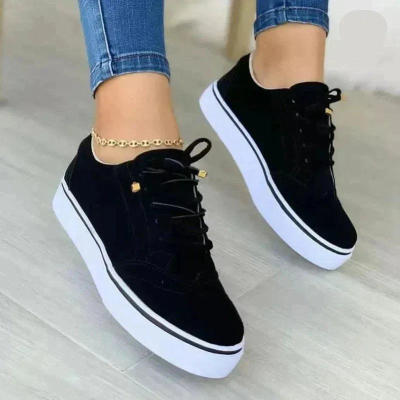 Black suede lace-up trainers with brogue stitching, gold eyelet caps and white platform sole, worn with jeans