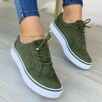 Olive green suede trainers shown from the front with brogue wingtip perforations and gold eyelets