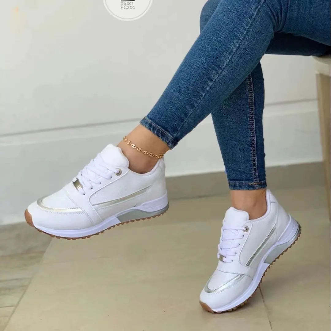 Side view of white trainers with gold-tone side stripe and chunky white sole worn by a seated model with jeans rolled up