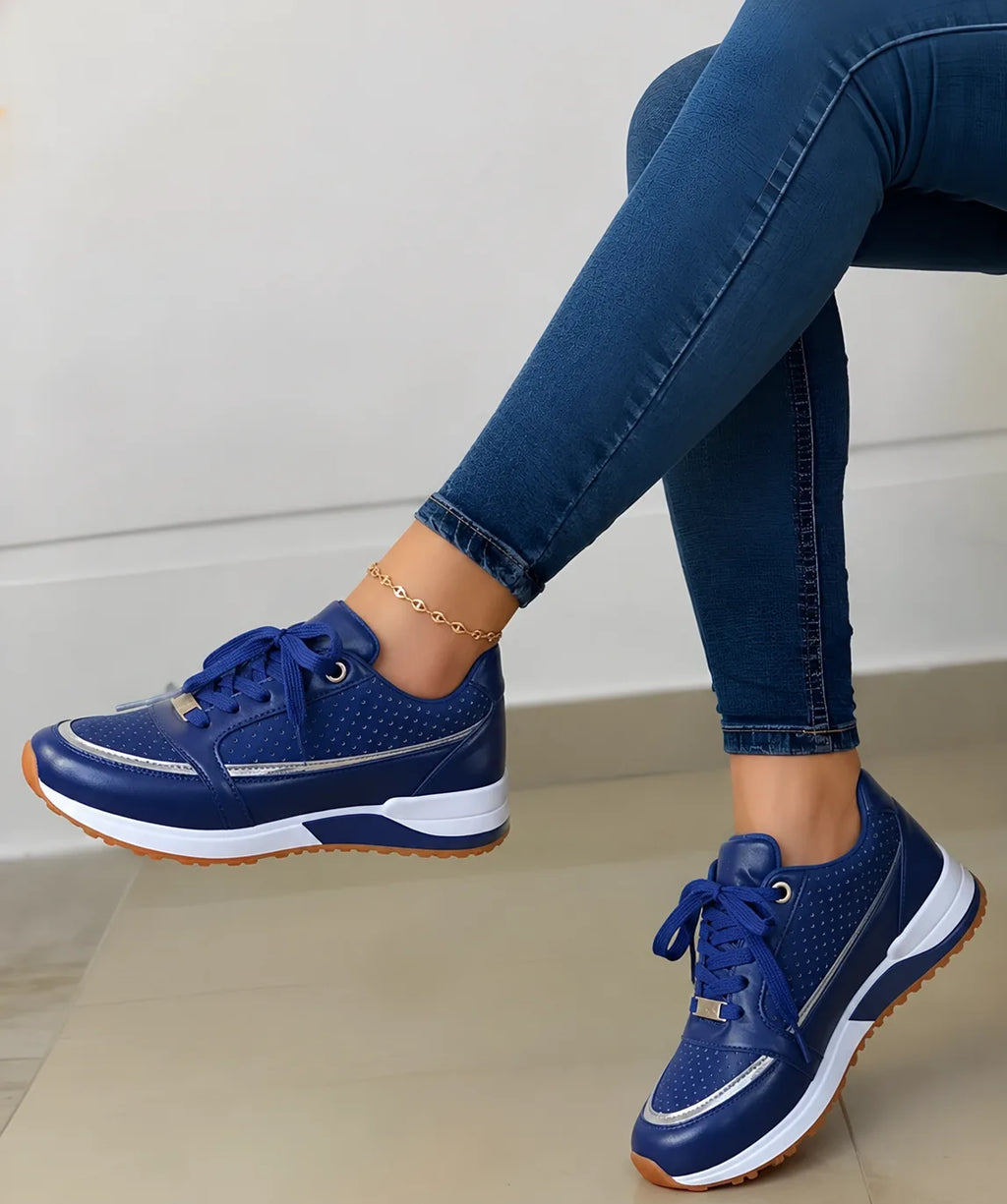 Side view of navy blue perforated trainer with white midsole and gum sole, worn by a seated model, gold-tone lace eyelets and heel tab.