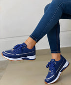 Side view of navy blue perforated trainer with white midsole and gum sole, worn by a seated model, gold-tone lace eyelets and heel tab.