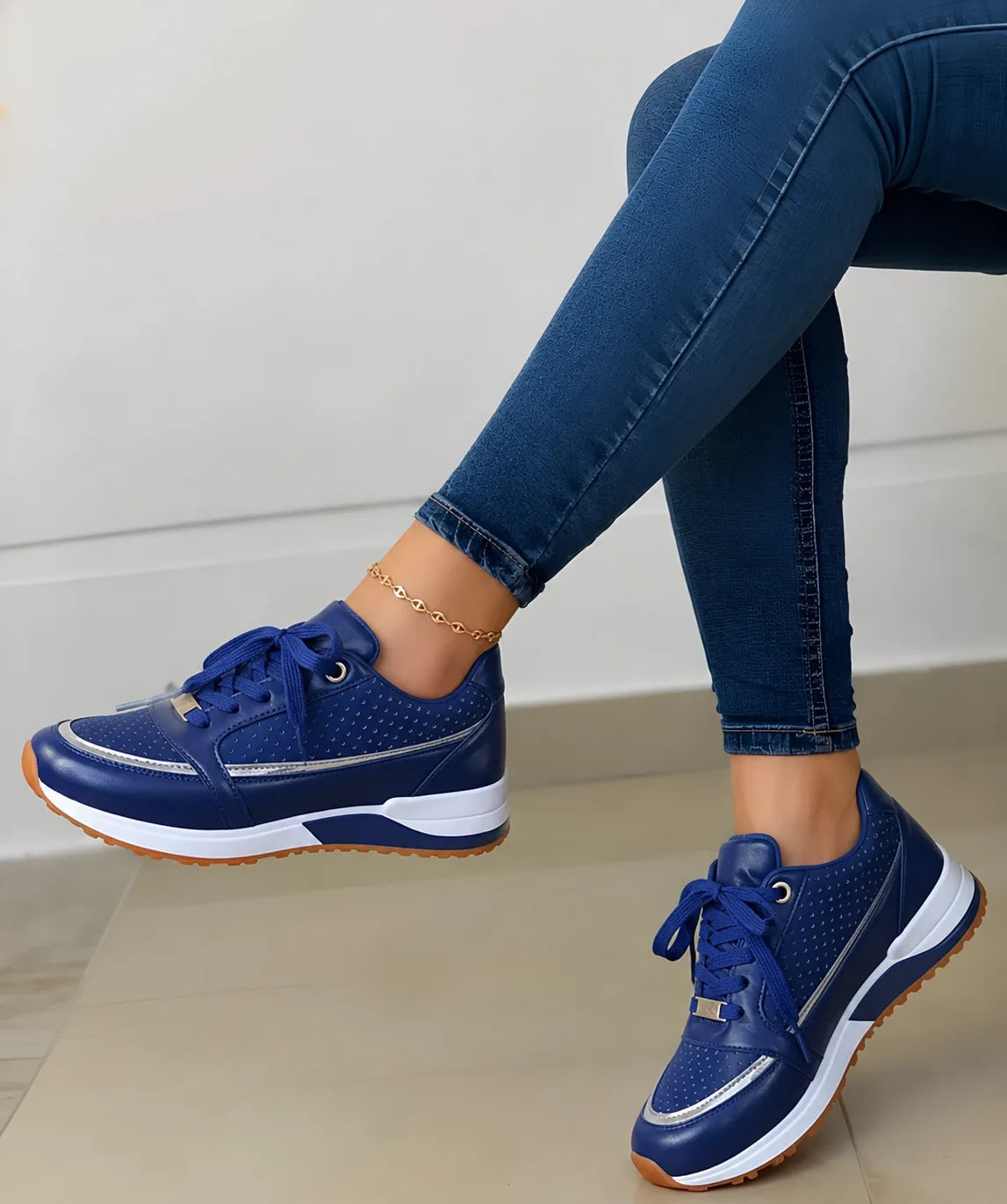 Side view of navy blue perforated trainer with white midsole and gum sole, worn by a seated model, gold-tone lace eyelets and heel tab.