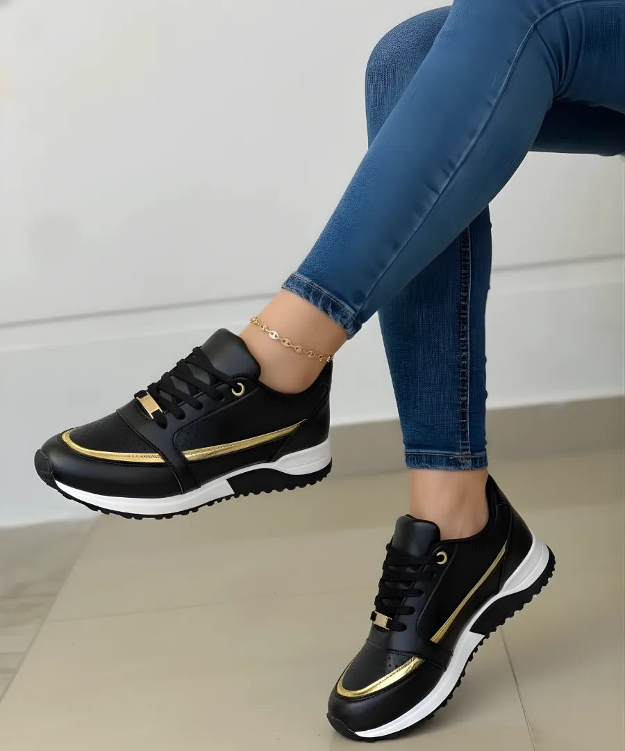 Black trainer with gold metallic side stripe and white platform sole, styled with skinny jeans and a gold anklet.