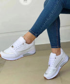 White trainer with silver metallic panelling and translucent sole detailing, shown from the side on a seated model.
