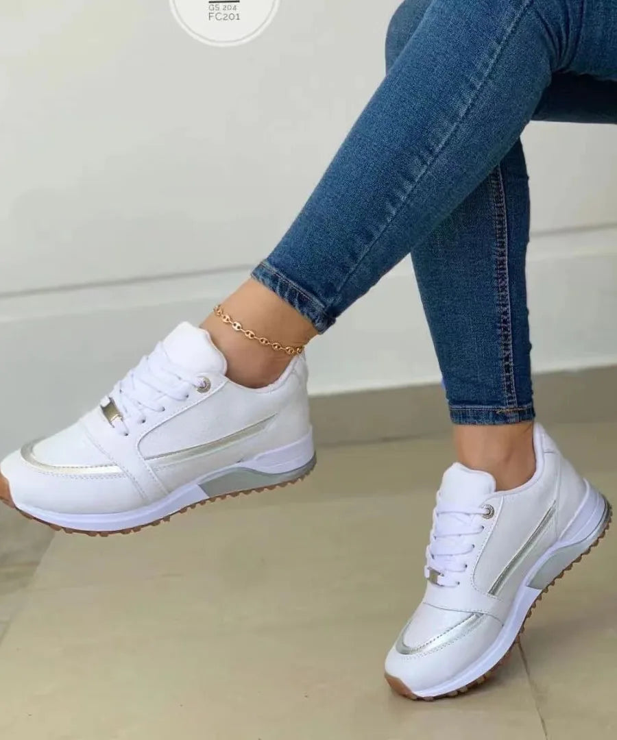 White trainer with silver metallic panelling and translucent sole detailing, shown from the side on a seated model.