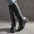 Side view of black knee-high leather boot with buckle strap detail and low block heel, worn with jeans