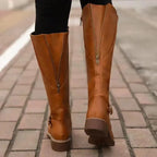 Back view of tan brown boots on cobbled street showing centre zip and buckle strap detail