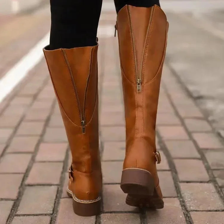 Back view of tan brown boots on cobbled street showing centre zip and buckle strap detail