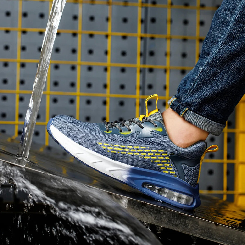 Side view of blue knit trainer with yellow accents worn under rolled denim jeans, rinsed by a stream of water on a metal surface