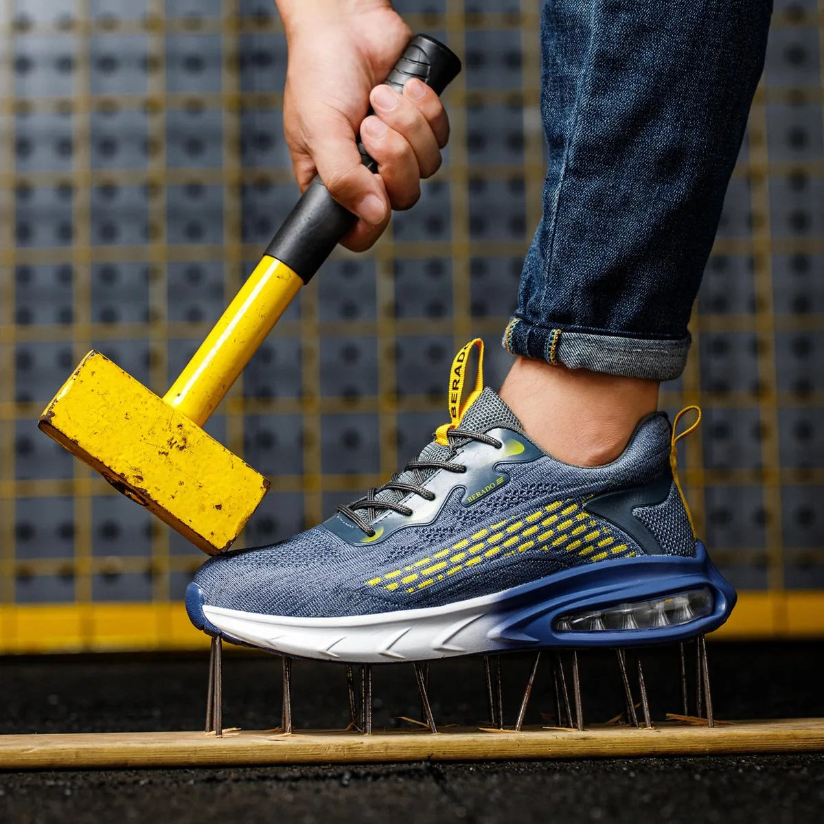 Blue trainer with yellow pull tab resting sole-up on a bed of nails while a mallet is held above it, demonstrating puncture resistance