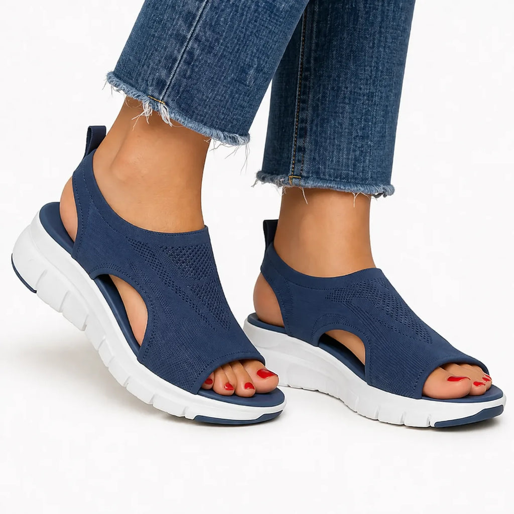 Side view of navy knit slip-on sandal with cutout sides, white chunky sole, worn with cropped jeans.