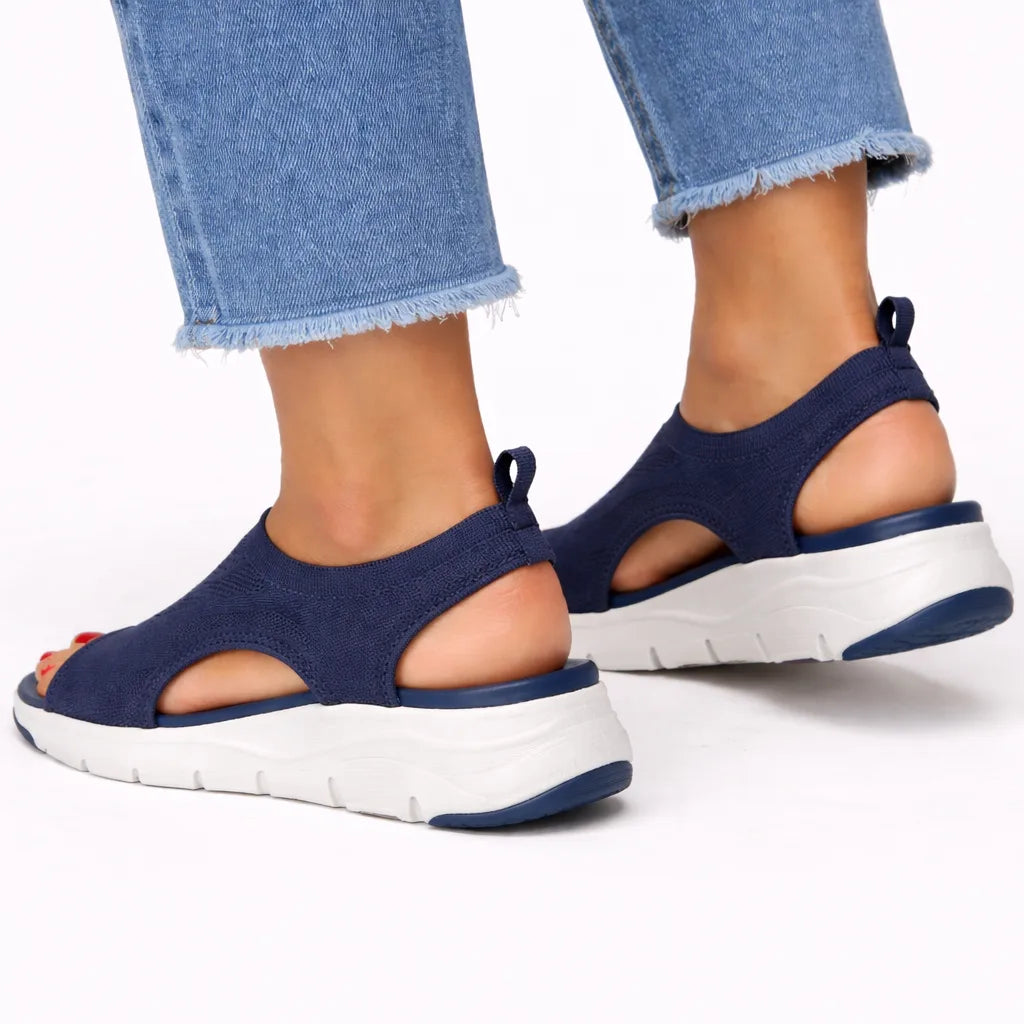 Rear three-quarter view of navy knit sandals showing heel pull tab, cutout sides and white ridged sole.
