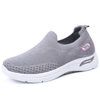 Side angle of a grey knit slip-on trainer with pink accent badge and white cushioned sole